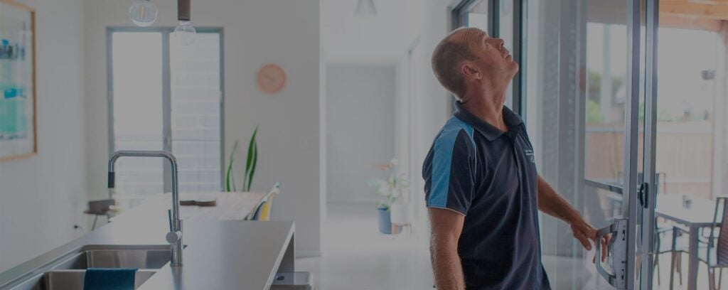 A man standing near a kitchen island, looking upward while inspecting a large glass sliding door leading outside.